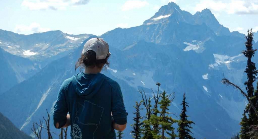 a person wearing a hat looks out over a mountainous landscape